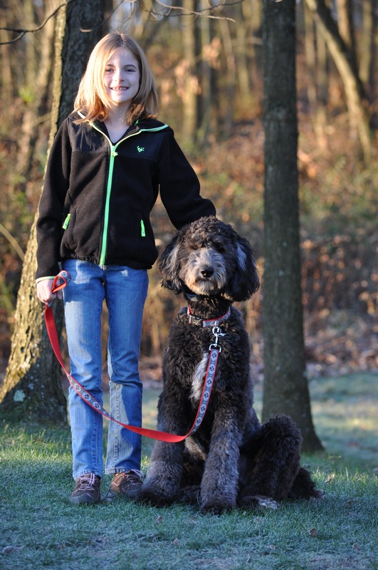 Young girl standing with her black goldendoodle in the woods